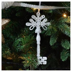 Close-up of a white glittery key-shaped ornament hanging on a festive Christmas tree