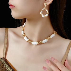 Close-up of twisted gold metal and white enamel jewelry set on an elegant model