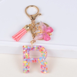 Detail view of resin letter R keychain with pink flower sequins, tassel, and butterfly charm