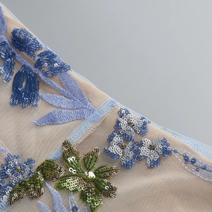 Detaillierte Makroansicht der floralen Stickerei mit blauen Pailletten auf beigem Tüll