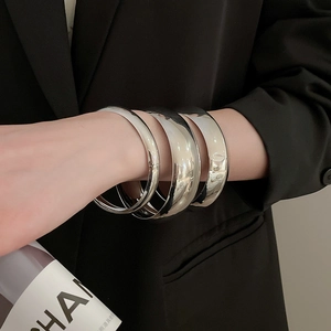 Détails de trois bracelets joncs minimalistes en argent polis sur une tenue noire