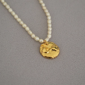 Macro shot of freshwater rice pearls and irregular golden coin pendant on a necklace
