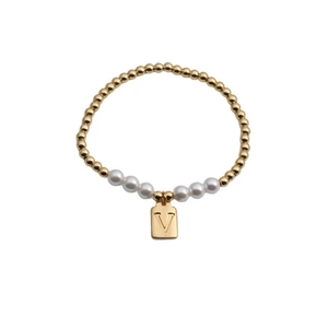 Detail of beaded bracelet with gold metal spheres, white pearls, and a letter V charm