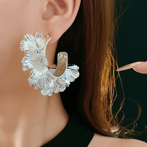 Macro detail of silver ginkgo leaf layered cluster hoop earrings on fashion model