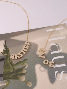 Detail von goldenen Buchstabenketten mit Zirkonia-Inlay und individuellen Anhängern