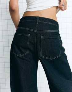 Detail view of high-waisted dark indigo wide leg jeans with yellow contrast stitching and back pockets