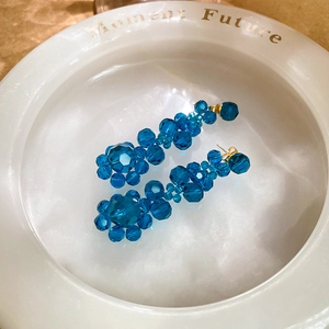 Close-up of blue crystal flower tassel earrings with golden pins in a white dish