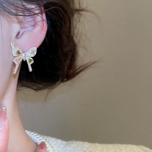 Macro detail of a butterfly stud earring with green heart stones and gold metal plating