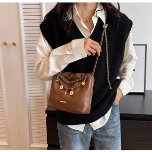 Close-up of brown quilted bucket bag with colorful charms and leather chain strap