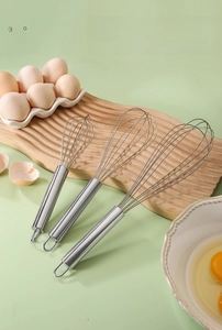Three-piece stainless steel whisk set with hanging hooks on a wooden tray with eggs