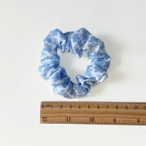 Floral light blue scrunchie with yellow details shown against a ruler for size