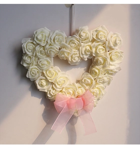 Détail d'une couronne de roses blanches en forme de cœur avec un nœud en organza rose