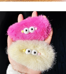Close-up of cute plush hair clips in pink and beige with funny cartoon eyes detail
