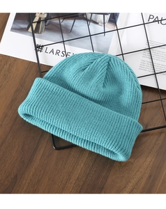 Close-up of teal ribbed knit beanie on a black mesh rack with a wood background