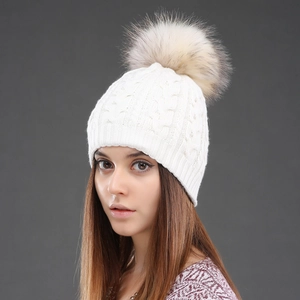 Close-up of white cable knit wool beanie with large fluffy fur pompom for winter