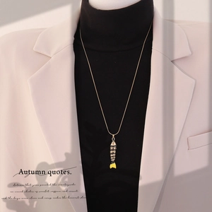 Detail of a vintage 3D koi fish pendant necklace worn over a black turtleneck sweater