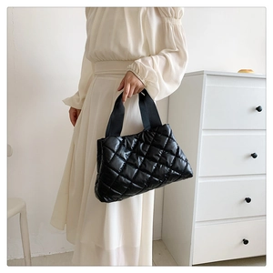 Détail d'un sac matelassé noir en nylon brillant avec une poignée large en ruban tissé