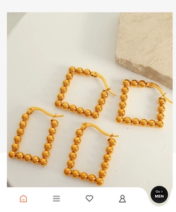 Detail of four golden geometric square bead earrings on a white stone background