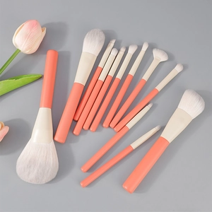 Flat lay of 13 coral orange makeup brushes with soft white bristles and pink tulip detail