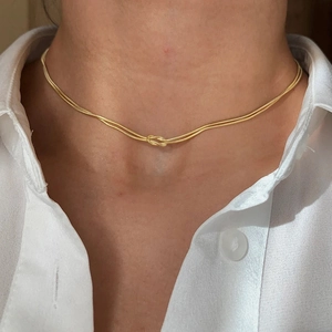 Close-up of golden double-layer snake chain necklace with a creative knotted central design