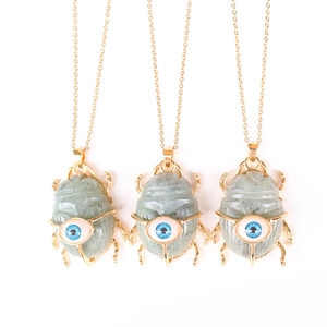 Three gold scarab necklaces with blue eye patterns and grey-green stones on white background