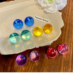 Detail of colorful resin ball stud earrings with silver needles on a rustic tray