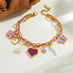 Golden butterfly and purple flower charm bracelet with heart pendants on stone background