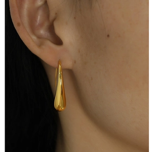 Detail of gold teardrop hook earrings with polished finish shown on a model