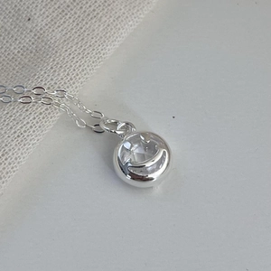Close-up of silver smiley face necklace with sparkling cubic zirconia on white fabric