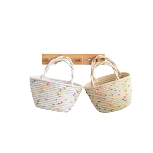 Handwoven cotton rope tote bag with colorful pom-poms shown on a wooden hook