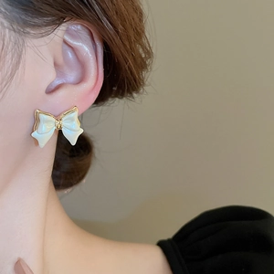 Close-up of bow knot stud earring with cream enamel inlay and elegant gold plating