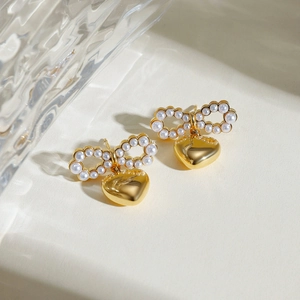 Macro view of gold bow earrings with pearl inlay and hanging heart pendants