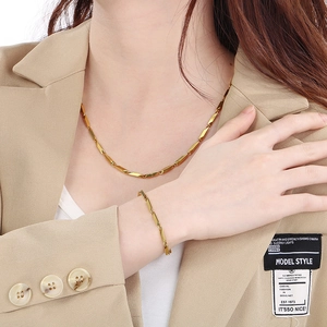 Close-up of golden geometric link necklace and bracelet set on a model in beige blazer