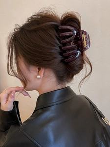 Detail of dark purple acrylic pumpkin stripe hair claw clip worn on a low bun hairstyle