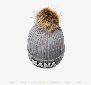 Close-up of dark grey knit hat with large brown faux fur pom and MAMA lettering
