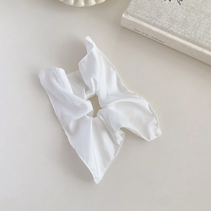 Flat lay of a white satin scrunchie next to a vintage book on a beige tabletop