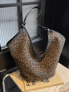 Large leopard print tote bag with black straps placed on books in a modern setting