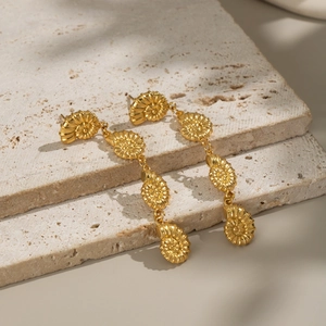 Detail view of golden nautilus shell long drop earrings on textured stone tiles