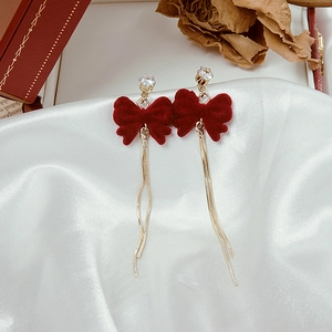 Detail of red velvet bow earrings with golden tassel chain and sparkling rhinestone studs