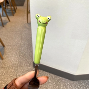 Close-up of a cartoon green frog handle on a polished stainless steel dessert spoon