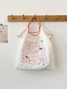 Detail of white embroidery tote bag with red piping and checkered orange handles
