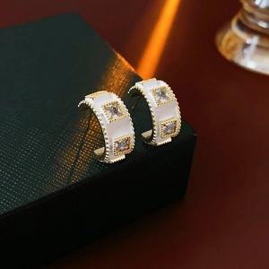 Detail of vintage C-shaped gold-plated earrings with white enamel and square gems