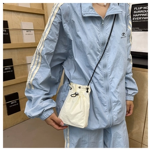 Detailed view of cream nylon drawstring bucket bag on a model in a casual setting