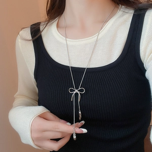 Detailed view of silver bow-knot long tassel necklace on black sweater worn by a model