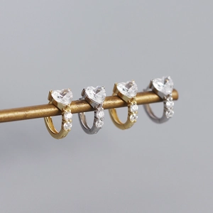 Macro detail of gold and silver heart-shaped zircon hoop earrings on a brass bar