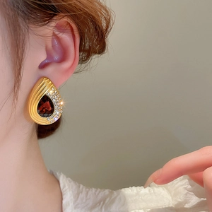 Close-up of golden teardrop earring featuring a large red gemstone and sparkling rhinestones