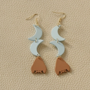 Detail of Halloween earrings featuring blue moons and brown bats on a textured surface