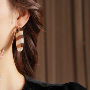 Detail of a C-shaped earring with striped wood grain resin on a model's ear