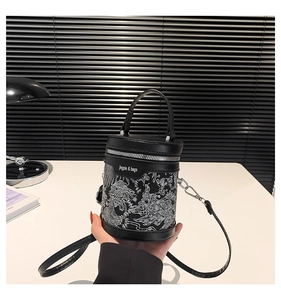 Detail of black cylinder bucket bag featuring white dragon prints and adjustable strap