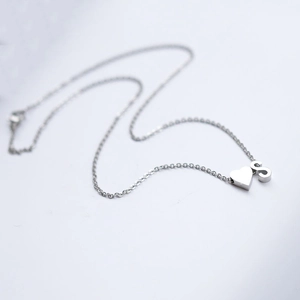 Detail shot of silver necklace featuring heart-shaped pendant and letter S charm
